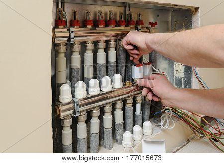 Installation of home heating. Men's hands attaches the servo valve drive underfloor heating.