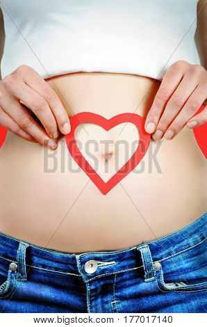 Woman holding a red heart shape around her navel on red background.
