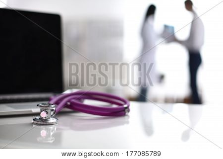Laptop and stethoscope on the desk , doctors standing in the background.