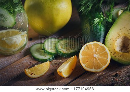 Background with assorted green vegetables: apple avocado cucumber lemon and detox water on rustic wooden table top. Healthy food detox dieting vegetarian and weightloss concept. Close up.