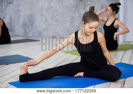 Shot of young women warming up before yoga session. Young people sitting on exercise mat in yoga class