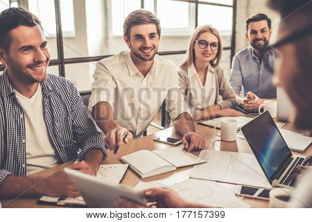 Successful young business people are using gadgets discussing documents and smiling during the conference