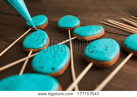 Preparing easter cookies with blue icing for decoration on rustic wooden table closeup