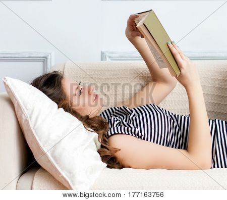 Young woman is lying on the sofa and reading book