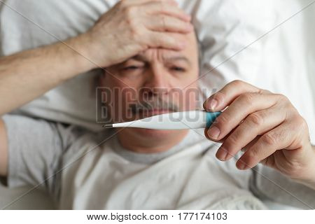 An elderly man measures the temperature with a thermometer. Heat and headache for colds or flu