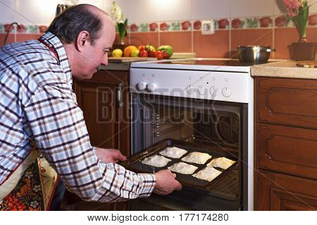 An Elderly Man In An Apron Prepares Pies At Home. A Hospitable Host Prepares Sweets For Guests