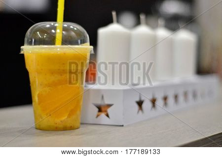 Natural orange juice in a plastic cup with straw, white tealight candles