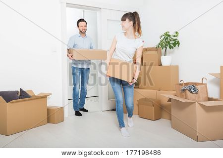 A young couple carrying boxes to new home. Moving makes them happy.