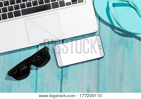 Work on the go. Modern laptop computer with smartphone and sunglasses on blue table, view from above