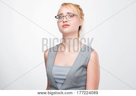 Young blonde woman looks shocked, stunned, taken aback and perplexed. Dumbfounded and bemused girl on grey background.