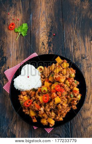 Picadillo a stew of ground beef and tomatoes with raisins and olives with boiled rice on a black plate. Wooden table top view.