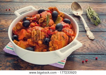 Chicken Cacciatore braised with wine and tomatoes traditional Italian dish. White casserole vintage spoon dry rosemary red pepper on the wooden rustic table.