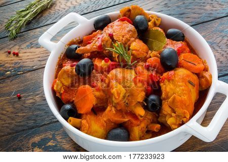 Chicken Cacciatore braised with wine and tomatoes traditional Italian dish. White casserole dry rosemary red pepper on the wooden rustic table.