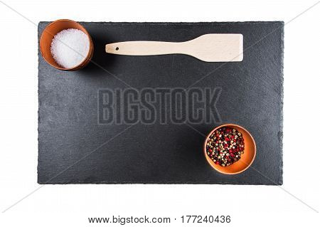 multicolored peppers and salt in a clay cup on a slate board wooden kitchen spatula top view isolated