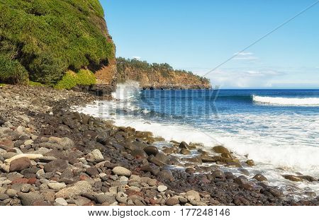 Surf crashes into rocky shore and cliffs of Kohala eroding cliffs. Cliffs along the north coast of the Big Island of Hawaii the Pacific ocean and blue sky with light clouds on a sunny day. View from Pololu Valley beach in February.