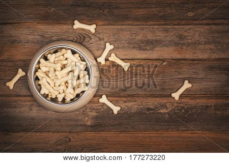 Top view of a bowl of crunchy boned shaped dog biscuits, on an old wooden floor. 