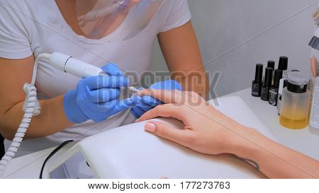 The master uses an electric machine to remove the nail polish on client hands during hardware manicure in the salon. Beauty and nail care concept