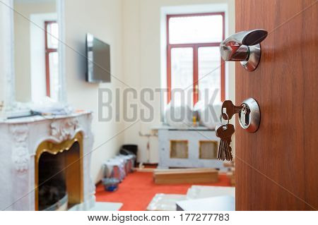 View on the opened door with keys in the lock and metall doorhandle of the apartment with fireplace during under renovation remodeling and construction.
