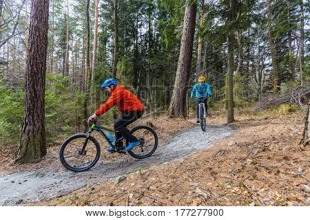 Mountain biking women and man riding on bikes in early spring mountains forest landscape. Couple cycling MTB enduro flow trail track. Outdoor sport activity.