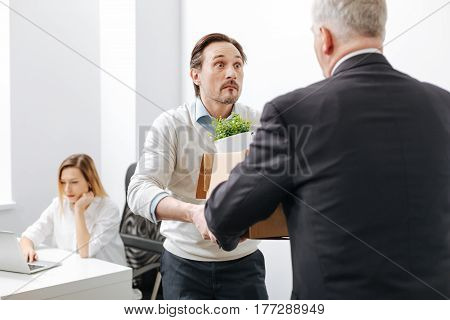 Shocking day of my life . Surprised puzzled perplexed employee standing and getting the box with belongings from employer while expressing astonishment