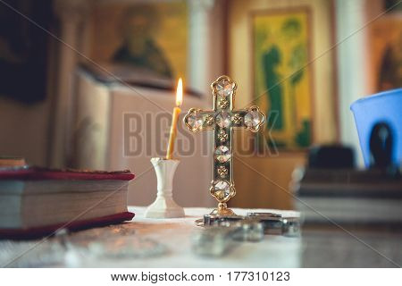 Cross gospel and candle on the background of icons in the Orthodox church