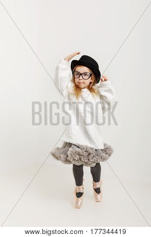Cute little girl hipster ballerina in a ballet tutu pointes glasses and a hat. The younger generation of dancers.