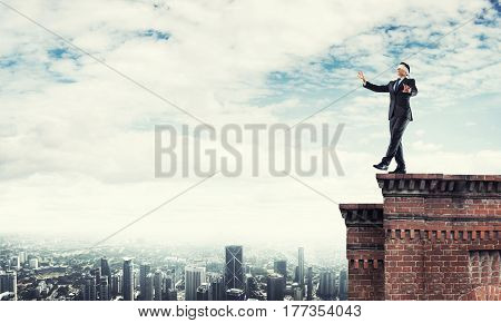 Businessman with blindfolder on eyes walking on building top