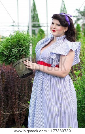 Young beautiful plus size Girl keeps pot with plant in the garden. Girl among the plants in the garden.