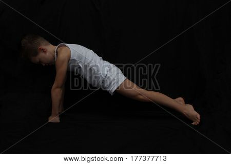 sport time. Young active caucasian white boy doing gymnastics isolsted on black background.a todler doing exercises for muscles.