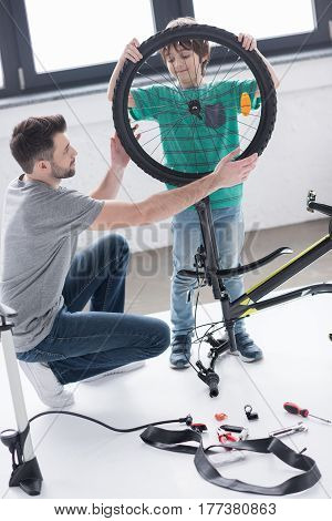 Father And Son Affixing Bicycle Wheel Together On White