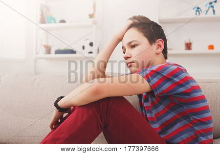 Unhappy lonely teenage boy at home, thinking about something, pubertal period, psychological problem. Lost in thoughts.