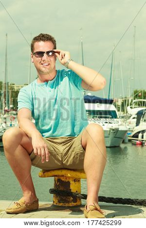 Summertime vacation adventure concept. Man spending his free time walking on marina sightseeing during summer guy sitting on bitt.