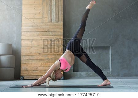 Young slim blond woman in yoga class making exercises. Girl do One-Legged Downward-Facing Dog Pose. Healthy lifestyle in fitness club. Stretching
