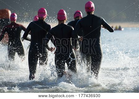Group triathlon participants running into the water for swim portion of race,splash of water and athletes running