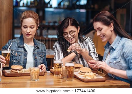 Being busy. Company of young women going to eat tasty burgers smiling while sitting next to each other