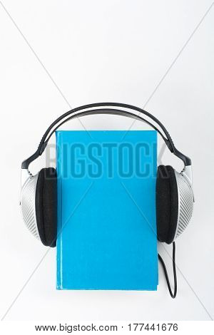 Audiobook on white background. Headphones put over blue hardback book empty cover copy space for ad text. Distance education e-learning concept