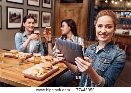 Turn on something. Delighted female person wearing jeans jacket holding her device in both hands while posing on camera