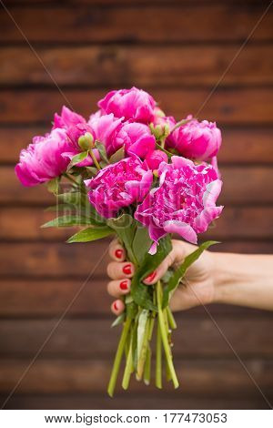 Beautiful bouquet of dark pink peonies in woman hands on a wooden background. Bunch of flowers in hands. Stripes. Summer time.