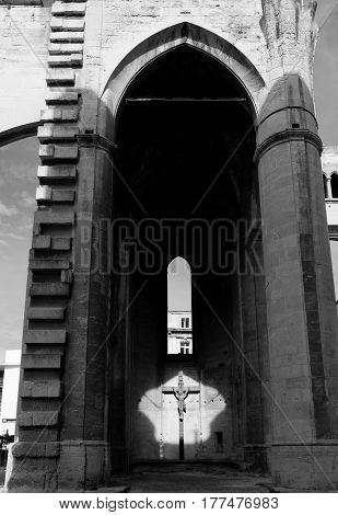 Cross with Jesus in arch highlighted by sun through opposing opening in monochrome Narbonne Cathedral architecture Cathedral of Saint-Just and Saint-Pasteur Narbonne France.