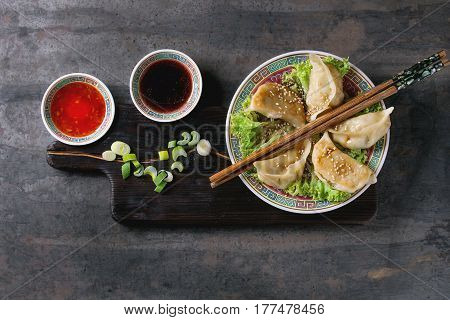 Gyozas potstickers on lettuce salad with sauces. Served in traditional china plate with chopsticks and spring onion on wood serving board over old metal background. Top view, space. Asian dinner