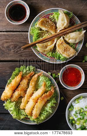 Fried tempura shrimps and gyozas potstickers on lettuce salad with sauces and rice. Served in traditional china plate with chopsticks over old wooden background. Top view. Asian dinner