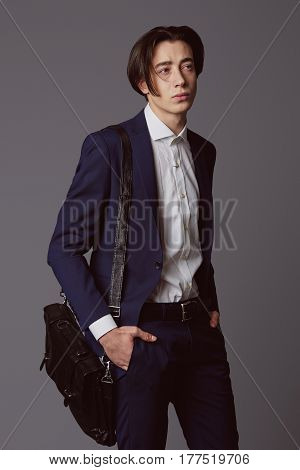 Business fashion man wearing blue suit with white shirt and bag on his shoulder. Studio shot against grey. Processed with VSCO s3 preset