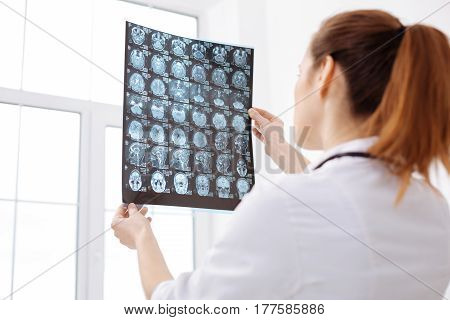 Many possibilities. Focused concerned trained neurosurgeon holding up and examining brain scans of the patient while working on his diagnosis