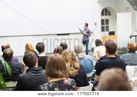 Male speaker giving presentation in lecture hall at university workshop. Audience in conference hall. Rear view of unrecognized participant. Scientific conference event. Copy space on whitescreen.
