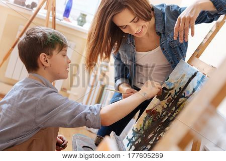 Enjoying art lesson . Delighted positive skilled teacher standing in the school and expressing joy while teaching painting child