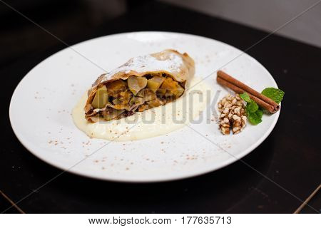 A piece of apetite strudel with orange, nut, cinnamon pod on a white plate