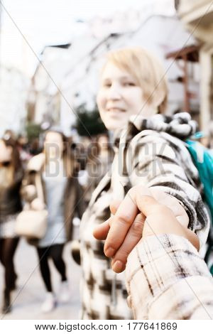 Cute excited Woman pulling someone hand and walking toward crowded city street. Casual clothing, blurred unrecognisable face