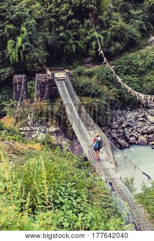 Woman backpacker crossing suspension bridge in Himalayas Nepal. Trekking and hiking with backpack in high mountains. Annapurna Himal Range on Annapurna Circuit Trek. Autumn season in Nepal Asia.