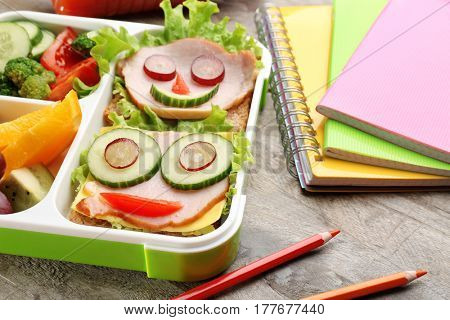 Funny sandwiches in lunch box and colorful stationery on wooden background