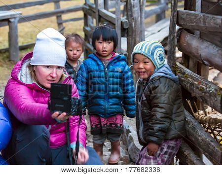 Western Woman taking Photo of little Nepalese Children in remote Himalaya Village expressing diverse emotions. Kothey Lodge, Nepal, Solo-Khumbu region, November 2, 2016